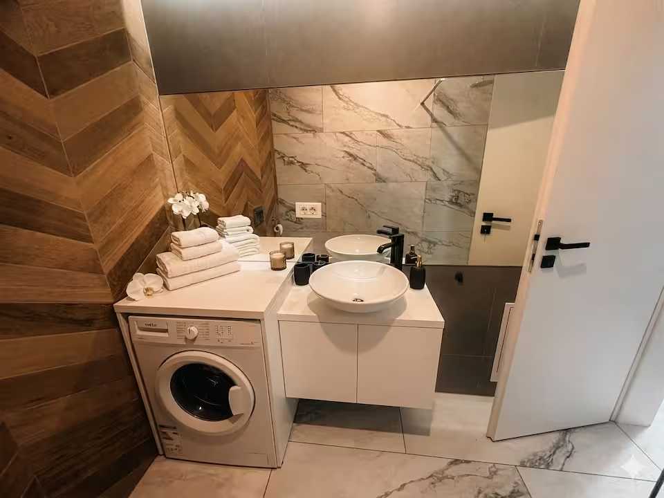 O baie cu o chiuvetă albă, o mașină de spălat și o oglindă — apartament în Oradea