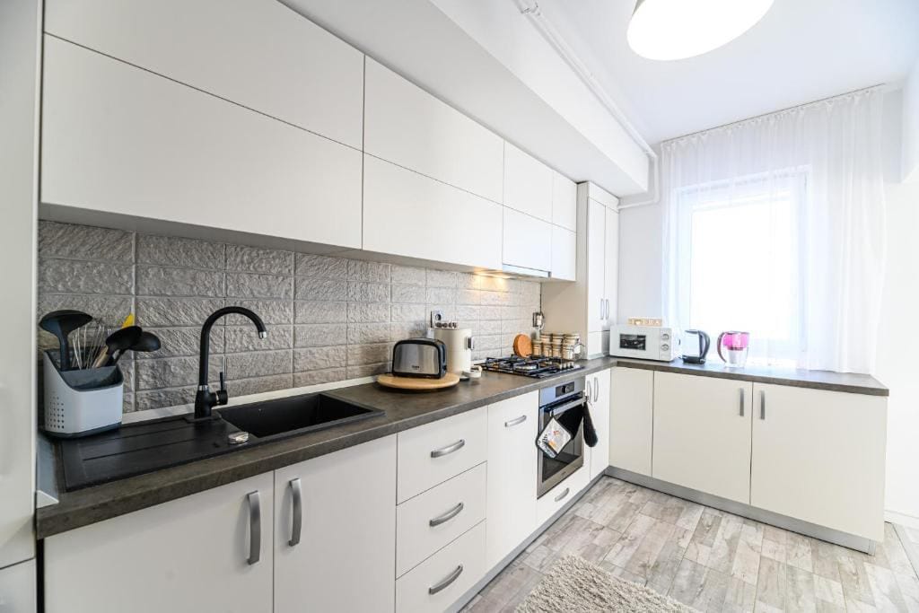 O bucătărie cu dulapuri albe și o fereastră — apartament în Brașov
