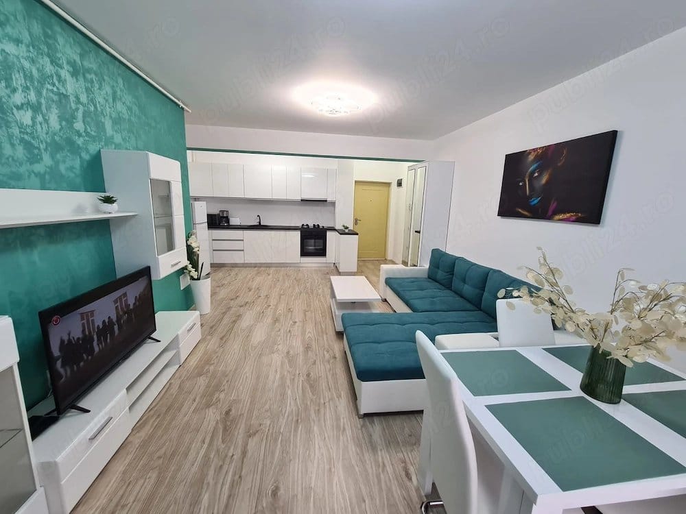 A living room with a couch, a table, a TV, and a view of a kitchen