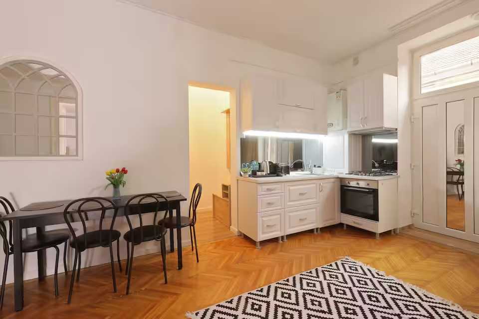 O bucătărie cu dulapuri albe și o masă — apartament în Oradea